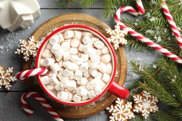 Tasty cocoa with marshmallows, candy canes, gingerbread cookies and Christmas decor on grey wooden table, flat lay
