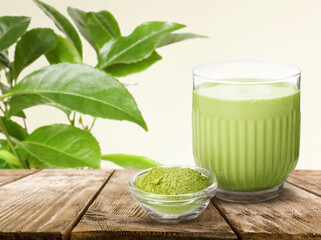 Matcha drink in glass and bowl with powder on wooden table against green leaves. Space for text