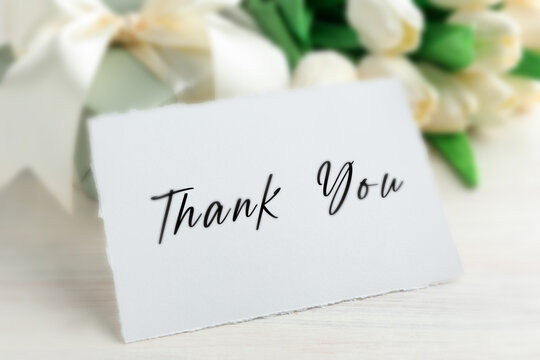 Thank You card and flowers on white wooden table, closeup