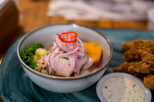 Peruvian ceviche with fish, onions, chili and corn served next to crispy fried fish and creamy dipping sauce on blue plate.