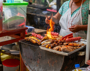 Peruvian Amazon street vendor grilling fish, chicken, plantains, and skewers over open flame in rustic outdoor food scene. © Productions