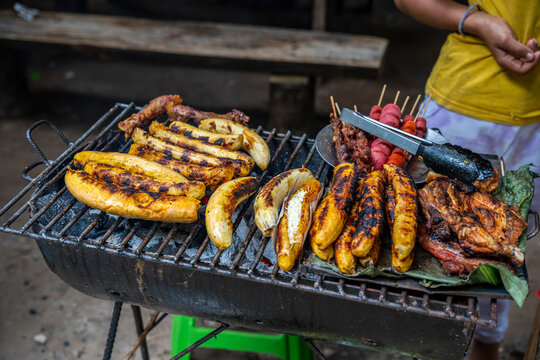 Plantains and chicken grilling on rustic charcoal barbecue in Peruvian Amazon street food environment.