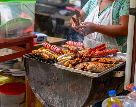 Peruvian Amazon street vendor grilling fish, chicken, plantains, and skewers over open flame in rustic outdoor food scene.