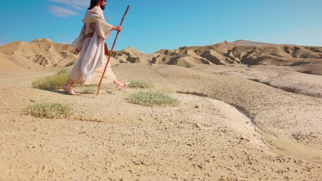 A lone figure stands atop a sandy hill under a clear blue sky. Slow motion shot