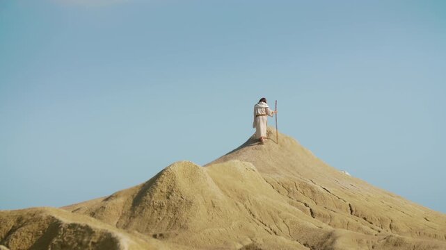 A robed Traveler ascension on a desert summit in slow motion. Christian and spiritual concept
