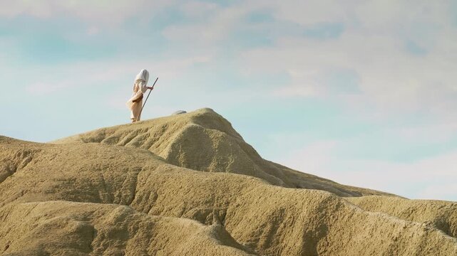 A Traveler in traditional robes stands on a desert summit. Christian and spiritual concept. Slow motion shot