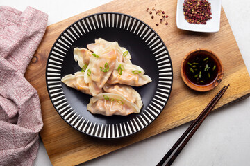 Elegant dumplings on a black plate with black chopsticks, napkin, and props on a white table. 