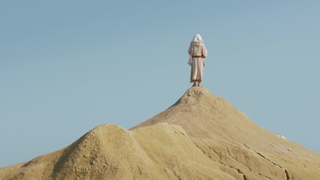 A robed Wanderer stands facing the horizon on a desert peak. Christian and spiritual concept