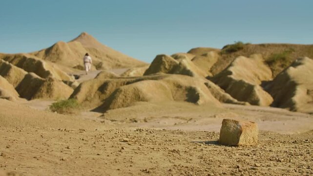Extreme Long Shot of a Solitary Traveler in simple traditional attire crosses an arid, sunlit terrain, using a wooden staff while walking through a quiet and rugged wilderness. Christian and spiritual