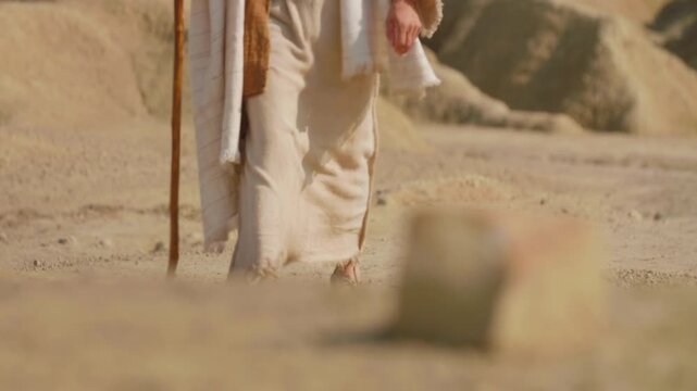 Jesus in ancient clothes walking alone on a dusty desert path. Christian and spiritual concept. Slow motion footage