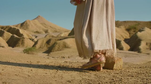 Close-up of feet and clothing as a Wanderer walks through an arid environment. Christian and spiritual concept