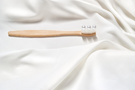 Eco friendly bamboo toothbrush with pearl like spheres arranged on white soft fabric creating a gentle minimal oral care concept symbolizing purity elegance, dental wellness