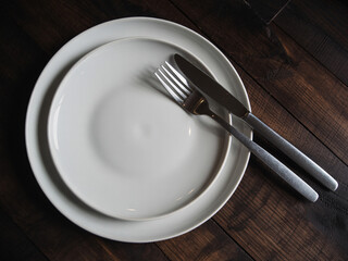 Elegant white dinner plates set with modern silverware resting on rich dark wood table ready for dining