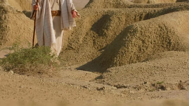 Detailed view of a person dressed in historical-style clothing walking through a dry, rocky landscape, illuminated by soft evening light. Christian and spiritual concept. Slow motion footage