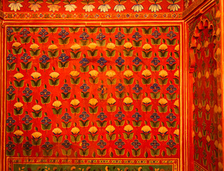 Rajasthani palace wall adorned with intricate floral patterns in vivid red, blue, green, and gold hues, showcasing traditional hand-painted artistry and royal decorative craftsmanship.