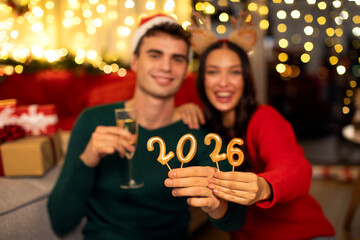 New Year 2026. Excited couple holding glasses of champagne and 2025 candles, celebrating holiday at...