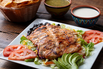 Mexican grilled chicken with vegetables and salad on a white plate and rustic wood table.