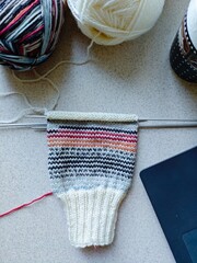 Knitting white sock with colorful stripes and yarn balls on workspace