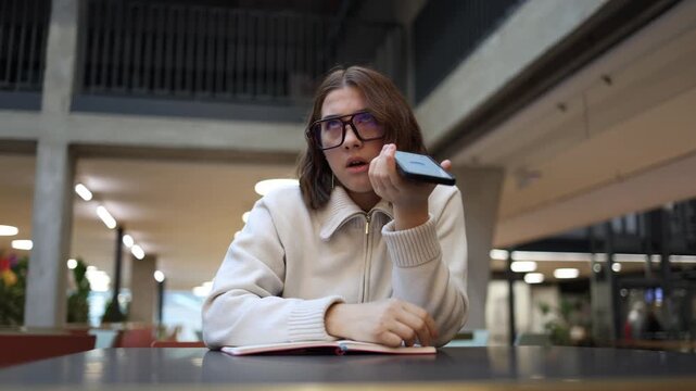 Woman rolls her eyes in frustration after another unhelpful answer from artificial intelligence while holding her phone in a modern study space reacting with tired disbelief