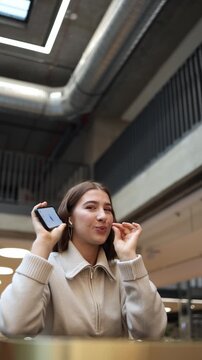 Vertical screen young woman smiles mischievously after artificial intelligence shares a secret and she makes a playful keep it quiet gesture enjoying the moment in a bright indoor space