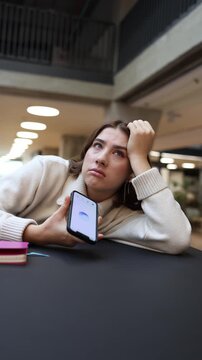 Vertical screen ChatGPT leaves the woman exhausted as she lies on the table holding her phone reacting with emotional frustration after hearing another unhelpful unclear answer 
