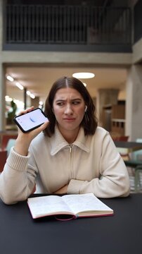 Vertical screen student hesitates while checking her homework answers with artificial intelligence holding her phone in doubt as the ai suggestions seem incorrect creating a moment of confusion 