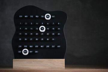 Modern black desk calendar with highlighted Friday 13th and October stands on wooden base against dark minimalist background.