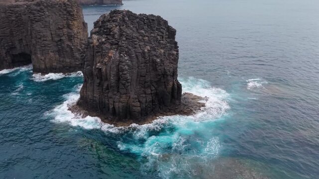 Turquoise ocean waves crashing against the stunning Roque Partido rock formation in Gran Canaria