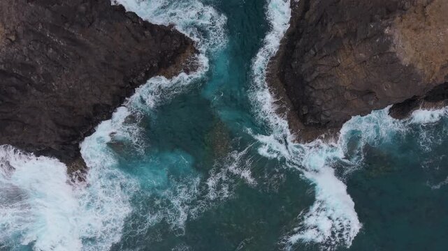 Majestic top down aerial view of ocean waves crashing against the volcanic cliffs of Gran Canaria