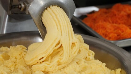 Minced boiled potatoes slowly emerge from meat grinder in production kitchen. Special mechanism creates thick mass during preparation stage for further processing into convenience food