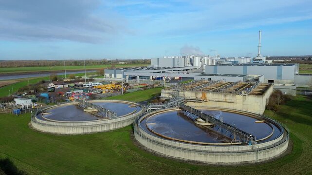 Aerial top-down drone view of industrial wastewater tanks with brown factory sewage, bubbling liquid surfaces, rotating sweep arms and mechanical filtration systems in Kings Lynn UK