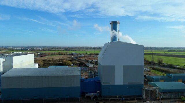 Aerial cinematic look at the Kings Lynn energy station featuring a high smoke stack chimney, exhaust vents and power generation infrastructure across the site