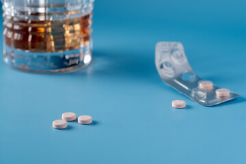 A blurred glass of alcohol in the background and a pack of pills. Three pink tablets are sitting on...