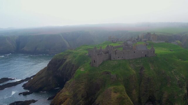 Aerial view of the medieval Dunnottar Castle ruin on a cliff during a foggy day in Scotland