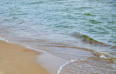 Transparent Baltic Sea water with small turquoise waves gently rolls onto smooth light sand, forming a calm diagonal shoreline and relaxed seaside mood