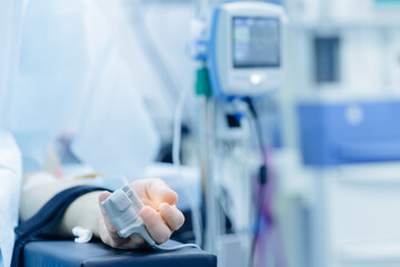 Close-up of hand with pulse oximeter in hospital setting with vital sign monitor