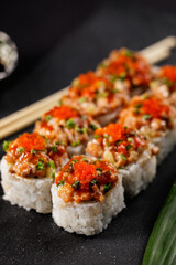 closeup of delicious sushi rolls with spicy toppings and chopsticks on black slate