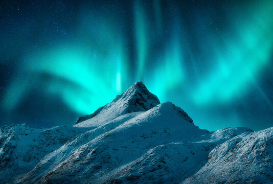 Northern lights over the snowy mountains at night in Lofoten, Norway. Aurora borealis above the snow covered rocks. Winter landscape with polar lights, mountain peak. Starry sky with green aurora