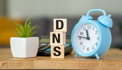 A blue alarm clock sits on a wooden table with a potted plant