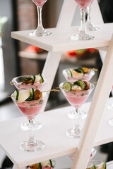 Elegant appetizers served in martini glasses with pink creamy base, garnished with cucumber, egg, herbs, and roasted vegetables—stylish gourmet presentation for events or catering.