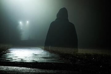 A spooky hooded ghost like figure on a path on an mysterious foggy winters night