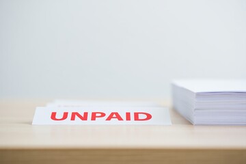 Unpaid red stamp notice beside a stack of invoices on a clean wooden desk