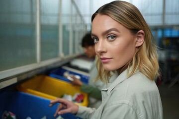 Determined woman with shoulder-length blonde hair sorting recyclables in facility