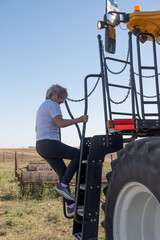 Mujera mayor subiendo al tractor en el campo