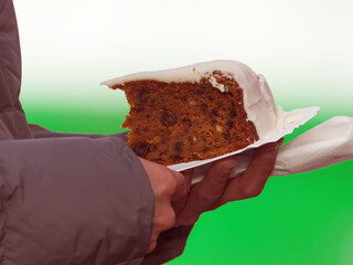 A person holding a slice of carrot cake with icing at the Naplavka farmers market in Prague, Czech Republic, during chilly autumn weather.