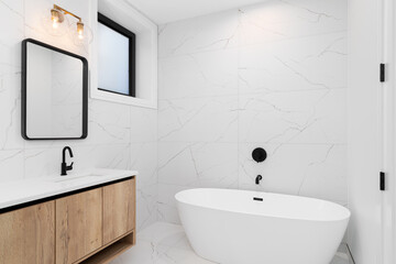 A bathroom detail with a white oak cabinet and white countertop, large format white marble tile...