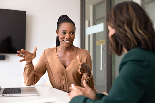 Positive young African manager explaining creative solution for business project to Caucasian partner, talking to female colleague at office table. Two diverse coworkers brainstorming on strategy
