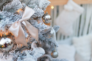 Close-up of elegant Christmas tree decoration with shiny silver ornaments and satin bow on flocked branch