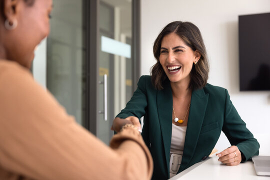 Cheerful satisfied young Hispanic businesswoman giving handshake to partner, project colleague, advisor, thanking for consultation meeting, teamwork, expertise, smiling, laughing, shaking hands