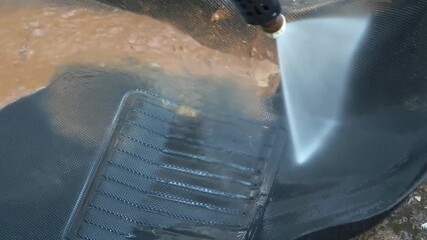 An industrial worker uses a power hose to clean dirt and debris from a surface, showcasing attention to cleanliness and maintenance.